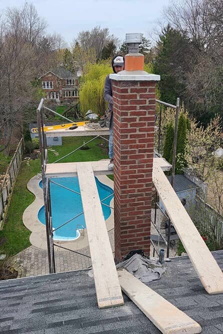 Mason rebuilding a chimney on scaffolding above a backyard pool